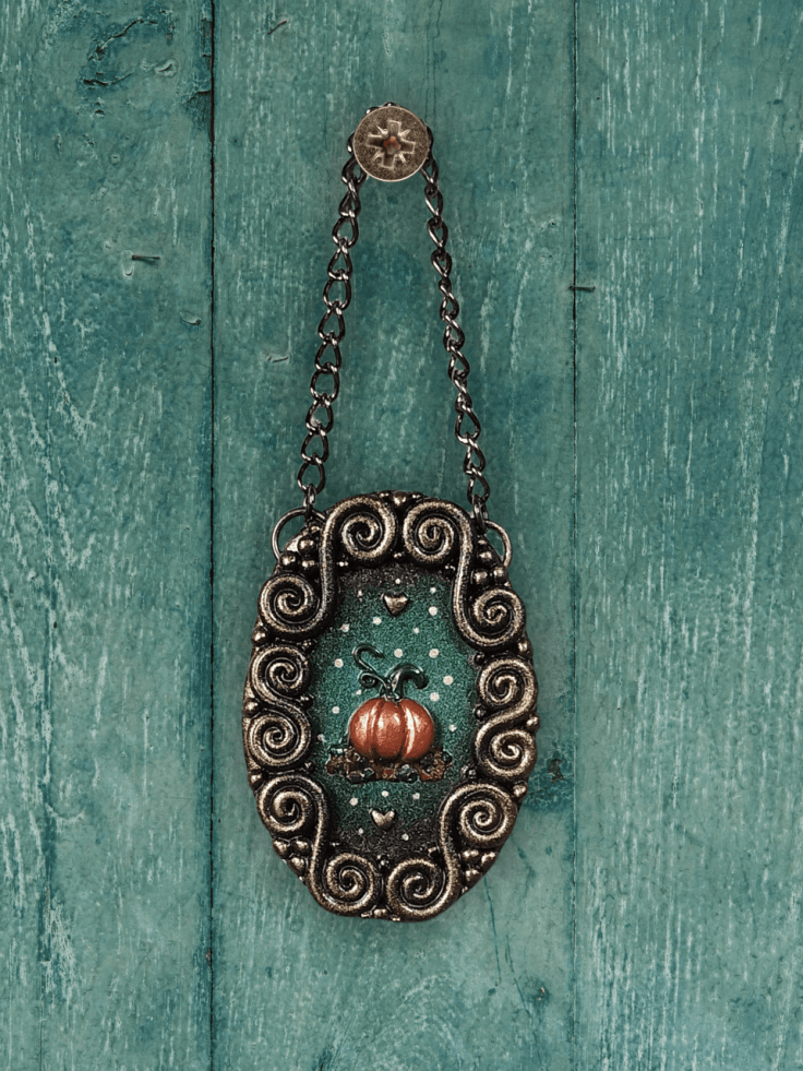 Mini pumpkin artwork hung up on the wall. The whole piece is made with polymer clay and features a mini pumpkin in the centre of an ornate frame