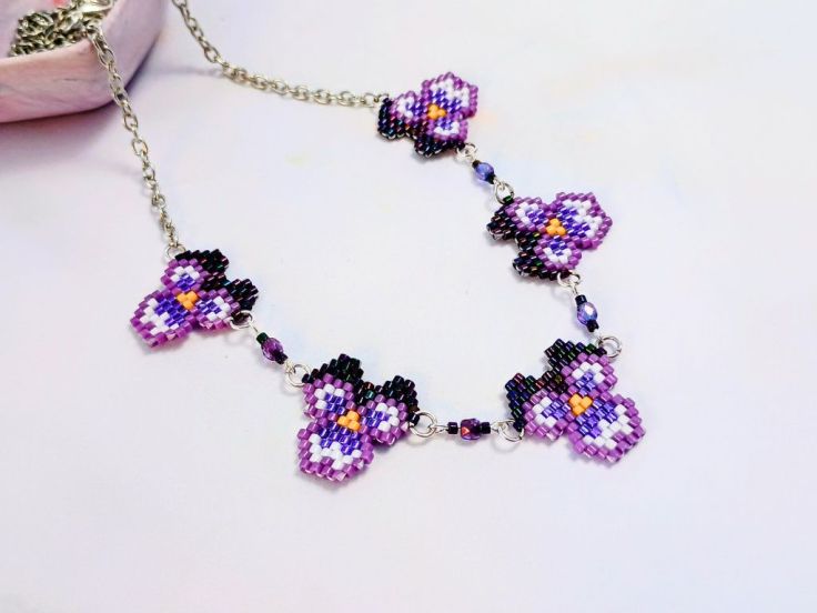 A necklace made with five brick stitch pansies on a silver chain
