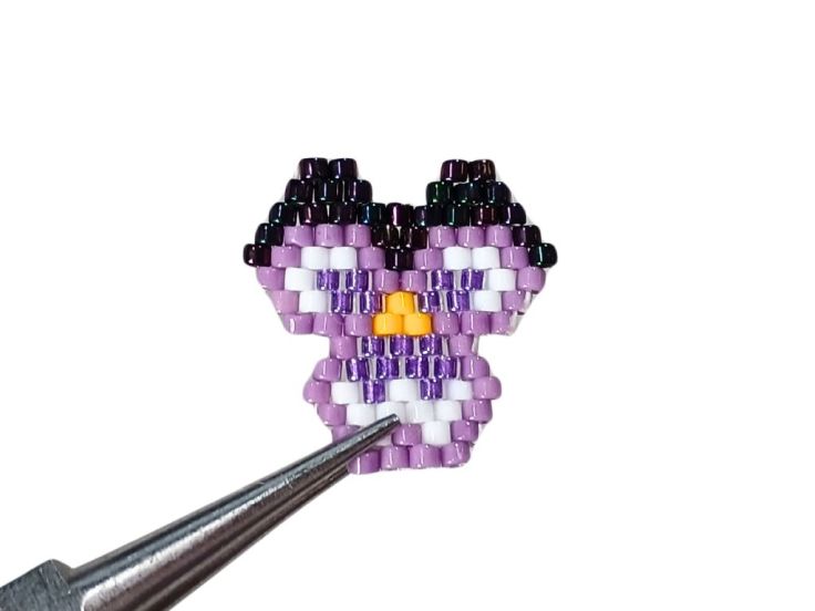 A close up of a single brick stitch pansy against a white background