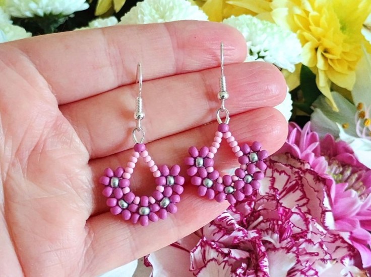 Seed bead flower earrings being held against a backdrop of fresh flowers
