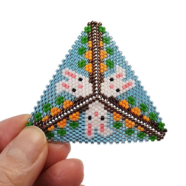 A peyote triangle featuring three white rabbits popping up in a carrot bed.