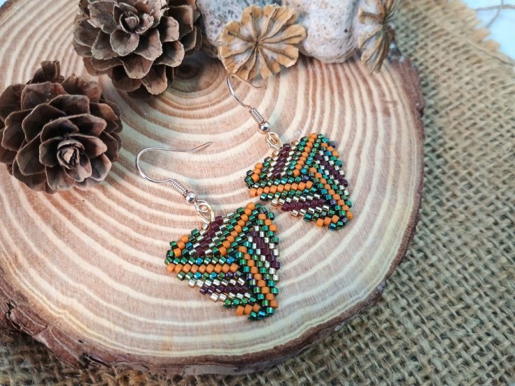 A picture of a pair of beaded peyote triangle earrings on an autumnal background. This photo is from a tutorial on how to read peyote triangle patterns.