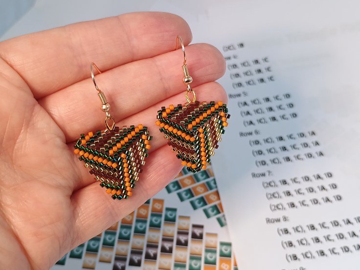 A pair of beaded peyote triangle earrings against a peyote triangle pattern
