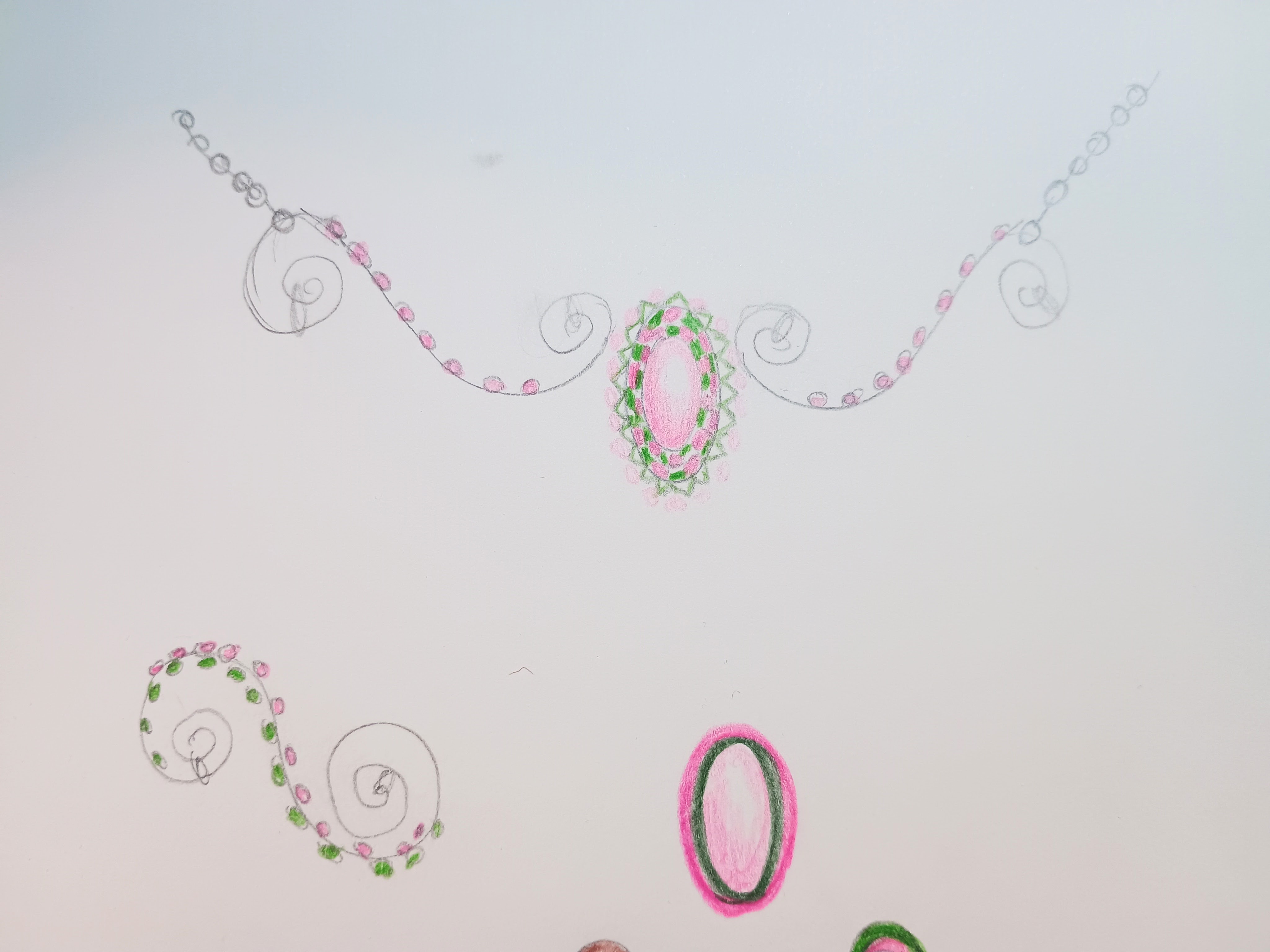 A detailed sketch of a necklace design featuring intricate swirls and floral patterns, with pink and green accents around an oval centerpiece.