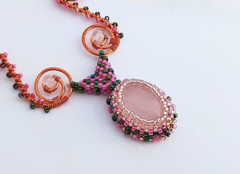 A close up of a rose quartz cabochon with a peyote beaded bezel and warped square bail.